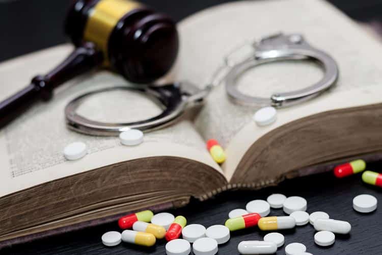 Different Drugs On The Table With Book, Gravel And Handcuffs