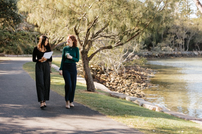 Two female legal professionals strolling down sidewalk surrounded by trees